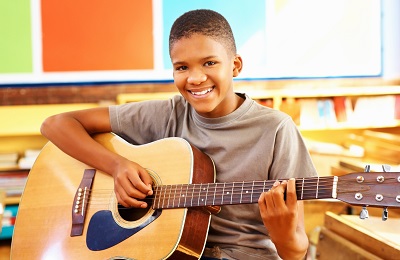 child with a smile holding a 
                      guitar 